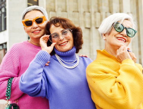 Three fashionable older adult women pose for the camera with sunglasses on.