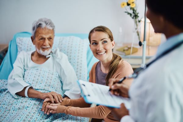 An older man in a hospital bed and his relative speak to his doctor
